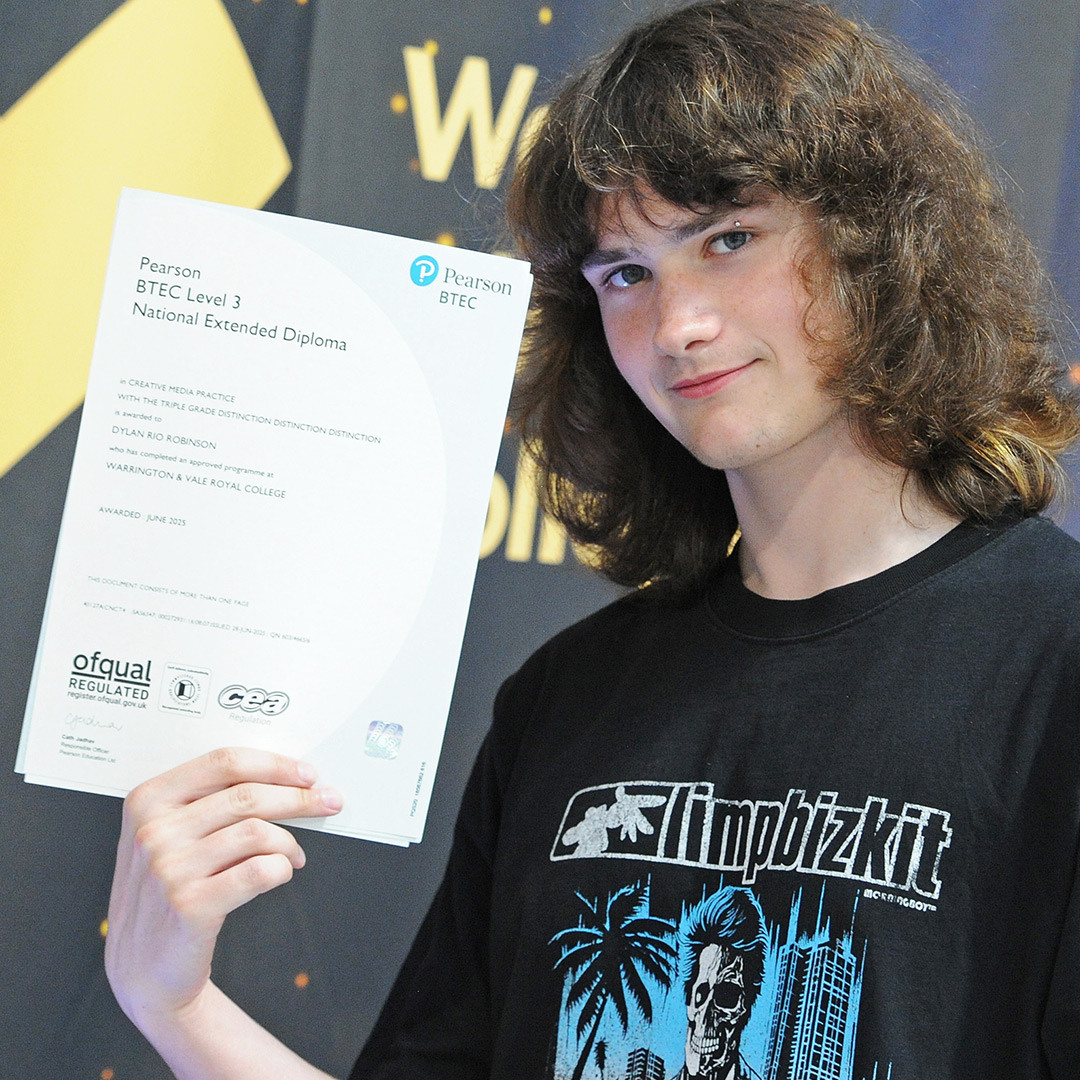 Student shows his triple distinction grade in front of photo backdrop
