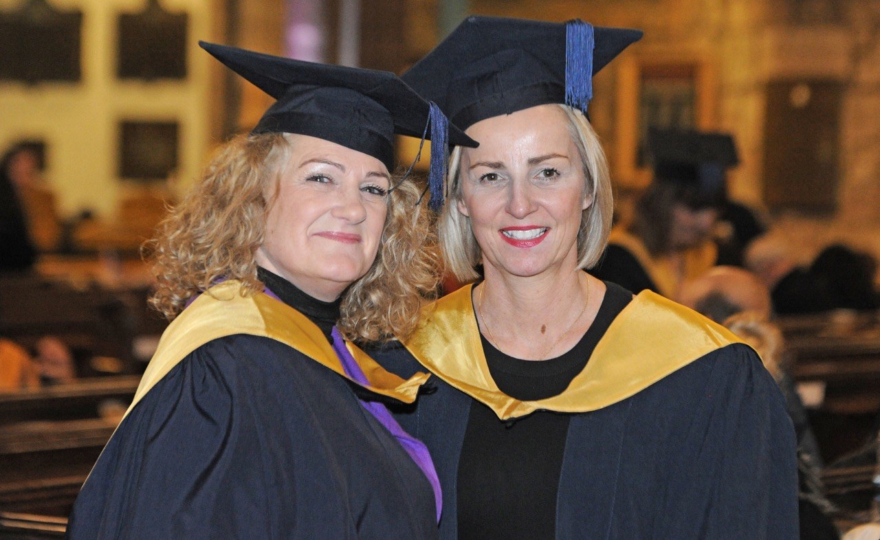 Two graduates smiling at camera with church background
